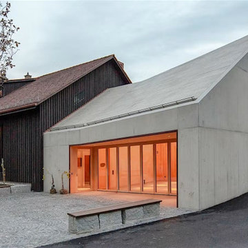 Concrete Facade with the Living Room Glowing Behind Glass, Berneck Residence