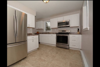 Example of a mid-sized l-shaped beige floor enclosed kitchen design with a drop-in sink, raised-panel cabinets, white cabinets, stainless steel appliances and no island
