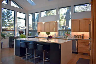 Contemporary l-shaped eat-in kitchen in Denver with flat-panel cabinets, light wood cabinets, stainless steel appliances, with island, medium hardwood floors and brown floor.