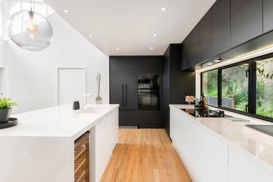 Inspiration for a large contemporary galley open plan kitchen in Auckland with an undermount sink, flat-panel cabinets, with island, white benchtop and black appliances.