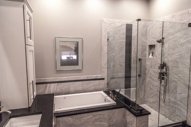 Example of a transitional master gray tile and ceramic tile marble floor, gray floor and double-sink bathroom design in Other with a two-piece toilet, gray walls, an undermount sink, quartzite countertops, a hinged shower door, black countertops and a niche