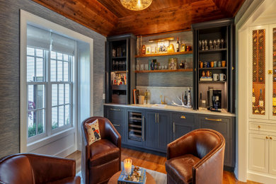 Inspiration for a large timeless single-wall medium tone wood floor and brown floor wet bar remodel in New York with a drop-in sink, recessed-panel cabinets, blue cabinets, marble countertops, beige backsplash, glass tile backsplash and beige countertops