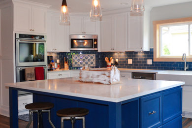 シカゴにあるお手頃価格の中くらいなカントリー風のおしゃれなキッチン (エプロンフロントシンク、シェーカースタイル扉のキャビネット、青いキャビネット、クオーツストーンカウンター、青いキッチンパネル、ガラスタイルのキッチンパネル、シルバーの調理設備、無垢フローリング、茶色い床、白いキッチンカウンター、三角天井) の写真