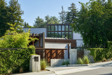 Example of a large minimalist gray two-story stucco exterior home design in San Francisco with a metal roof and a brown roof