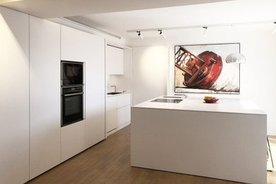 Foto di una cucina contemporanea di medie dimensioni con lavello da incasso, ante lisce, ante bianche, top in superficie solida, paraspruzzi bianco, pavimento in legno verniciato, pavimento marrone e top bianco