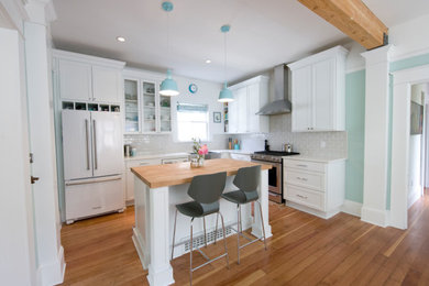 This is an example of a mid-sized country l-shaped eat-in kitchen in Portland with a farmhouse sink, recessed-panel cabinets, white cabinets, quartz benchtops, grey splashback, ceramic splashback, white appliances, medium hardwood floors, with island, brown floor and white benchtop.