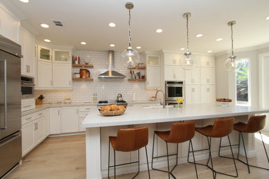 Inspiration for a large transitional l-shaped open plan kitchen in Orange County with a farmhouse sink, shaker cabinets, white cabinets, quartz benchtops, white splashback, subway tile splashback, stainless steel appliances, light hardwood floors, with island and beige floor.
