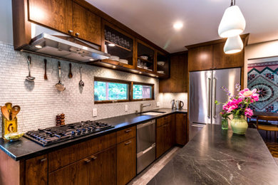 This is an example of a small traditional l-shaped separate kitchen in Minneapolis with an undermount sink, flat-panel cabinets, dark wood cabinets, soapstone benchtops, white splashback, stainless steel appliances, with island, grey floor and black benchtop.