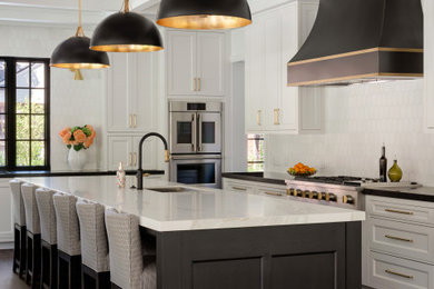 Example of a large classic medium tone wood floor, brown floor and coffered ceiling eat-in kitchen design in Dallas with an undermount sink, recessed-panel cabinets, white cabinets, granite countertops, white backsplash, stone tile backsplash, stainless steel appliances, an island and black countertops