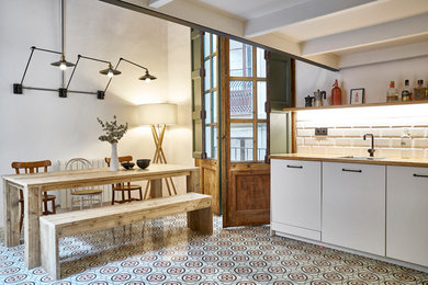 This is an example of a mid-sized modern l-shaped eat-in kitchen in Barcelona with a drop-in sink, flat-panel cabinets, white cabinets, wood benchtops, white splashback, ceramic splashback, stainless steel appliances, terra-cotta floors, no island and multi-coloured floor.