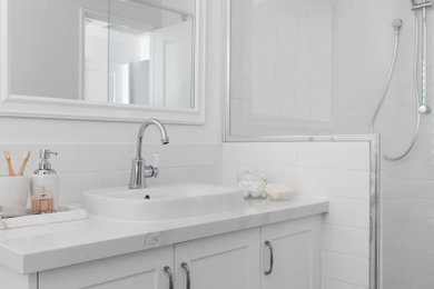 パースにあるビーチスタイルのおしゃれな浴室 (シェーカースタイル扉のキャビネット、白いキャビネット、置き型浴槽、コーナー設置型シャワー、白いタイル、セラミックタイル、白い壁、磁器タイルの床、オーバーカウンターシンク、クオーツストーンの洗面台、青い床、開き戸のシャワー、白い洗面カウンター、洗面台1つ、造り付け洗面台) の写真