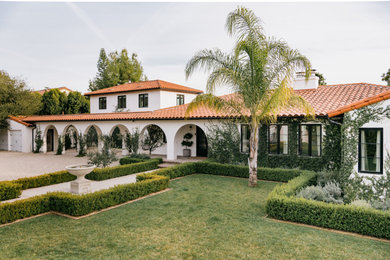 This is an example of a large mediterranean two-storey stucco white house exterior in Los Angeles with a gable roof, a tile roof and a red roof.