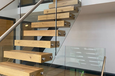 This is an example of a wood floating glass railing staircase in Essex with wood risers.