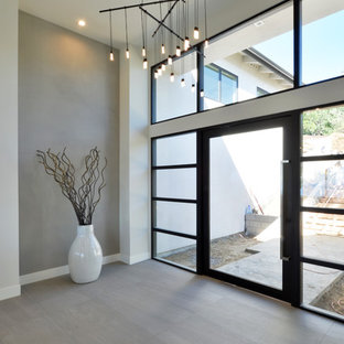 На фото: огромное фойе в стиле модернизм с белыми стенами, поворотной входной дверью, стеклянной входной дверью и полом из керамогранита с