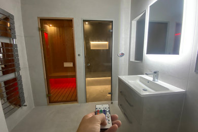 This is an example of a medium sized modern grey and white sauna bathroom in Other with a built-in shower, a wall mounted toilet, grey tiles, ceramic tiles, grey walls, ceramic flooring, a wall-mounted sink, grey floors, a hinged door, feature lighting, a single sink and a floating vanity unit.