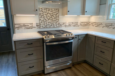Large minimalist l-shaped laminate floor and brown floor eat-in kitchen photo in Other with an undermount sink, raised-panel cabinets, gray cabinets, quartzite countertops, gray backsplash, glass tile backsplash, stainless steel appliances, a peninsula and white countertops
