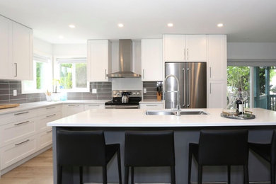 Example of a mid-sized transitional l-shaped laminate floor and beige floor open concept kitchen design in Vancouver with an undermount sink, shaker cabinets, white cabinets, quartz countertops, gray backsplash, porcelain backsplash, stainless steel appliances, an island and gray countertops