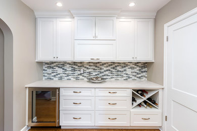 Example of a mid-sized classic single-wall medium tone wood floor home bar design in Chicago with no sink, shaker cabinets, white cabinets, quartz countertops, gray backsplash and glass tile backsplash