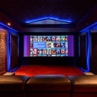 Cette photo montre une grande salle de cinéma tendance fermée avec moquette, un téléviseur encastré, un mur multicolore et un sol rouge.