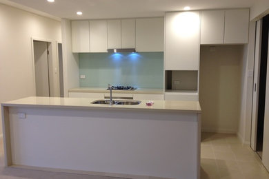 This is an example of a mid-sized modern galley eat-in kitchen in Sydney with an undermount sink, recessed-panel cabinets, white cabinets, quartz benchtops, green splashback, glass sheet splashback, stainless steel appliances, ceramic floors and with island.