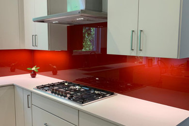 Kitchen - contemporary kitchen idea in Detroit with flat-panel cabinets, red backsplash, glass sheet backsplash, an island and white countertops