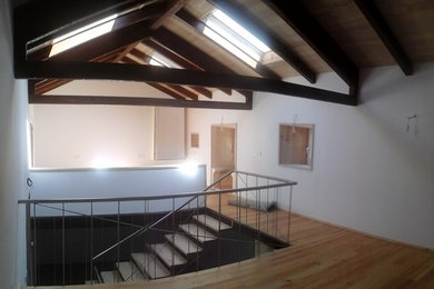 Foto de dormitorio tipo loft de tamaño medio con paredes blancas, suelo de madera clara y marco de chimenea de piedra