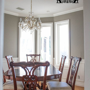 Idée de décoration pour une salle à manger tradition fermée et de taille moyenne avec un mur gris, un sol en bois clair, cheminée suspendue et un sol marron.