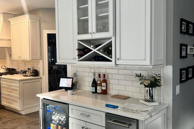 Photo of a large l-shaped eat-in kitchen in New York with an undermount sink, flat-panel cabinets, white cabinets, quartz benchtops, white splashback, subway tile splashback, stainless steel appliances, porcelain floors, with island, grey floor and white benchtop.