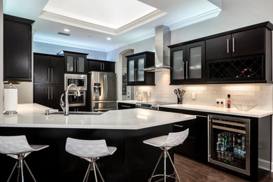 Photo of a contemporary u-shaped kitchen/diner in Miami with a submerged sink, flat-panel cabinets, black cabinets, white splashback, stainless steel appliances, dark hardwood flooring, a breakfast bar, brown floors, white worktops and a drop ceiling.