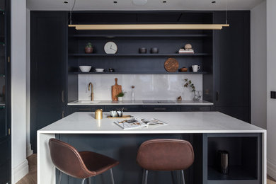Contemporary open plan kitchen in London with quartz worktops, white splashback, engineered quartz splashback, integrated appliances, an island, white worktops, a submerged sink, shaker cabinets, black cabinets, medium hardwood flooring and brown floors.