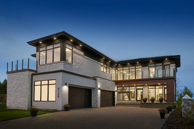 Photo of a large contemporary two-storey stucco beige house exterior in Edmonton with a gable roof and a shingle roof.