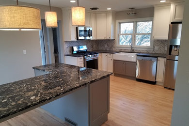 Eat-in kitchen - light wood floor eat-in kitchen idea in Grand Rapids with a farmhouse sink, granite countertops, gray backsplash, ceramic backsplash, stainless steel appliances and an island