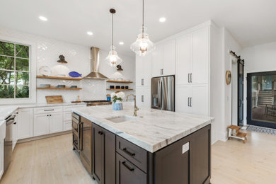 Large transitional l-shaped light wood floor and beige floor eat-in kitchen photo in Charleston with a farmhouse sink, flat-panel cabinets, white cabinets, quartzite countertops, white backsplash, ceramic backsplash, stainless steel appliances, an island and multicolored countertops