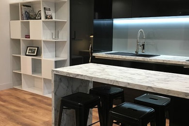 Aménagement d'une petite cuisine américaine encastrable contemporaine en U avec un évier 1 bac, un placard à porte affleurante, des portes de placard noires, un plan de travail en stratifié, une crédence grise, une crédence en feuille de verre, îlot, un sol marron et un plan de travail multicolore.