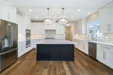 Example of a large classic u-shaped medium tone wood floor and brown floor kitchen design in Chicago with white cabinets, granite countertops, multicolored backsplash, stainless steel appliances, an island and white countertops