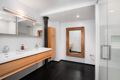 Mid-sized trendy master white tile and porcelain tile porcelain tile, black floor and double-sink corner shower photo in New York with light wood cabinets, white walls, an integrated sink, quartzite countertops, a hinged shower door, white countertops and a niche