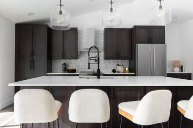 Example of a mid-sized trendy single-wall vinyl floor, brown floor and vaulted ceiling open concept kitchen design in Seattle with an undermount sink, shaker cabinets, dark wood cabinets, quartz countertops, multicolored backsplash, marble backsplash, stainless steel appliances, an island and white countertops