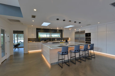 Photo of a large modern l-shaped eat-in kitchen in Los Angeles with a single-bowl sink, flat-panel cabinets, white cabinets, marble benchtops, grey splashback, subway tile splashback, stainless steel appliances, concrete floors and with island.