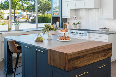 Modern eat-in kitchen in Vancouver with a farmhouse sink, shaker cabinets, blue cabinets, quartz benchtops, white splashback, stainless steel appliances, with island and grey benchtop.