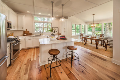 Photo of a mid-sized arts and crafts l-shaped open plan kitchen in Indianapolis with white cabinets, stainless steel appliances, medium hardwood floors and with island.