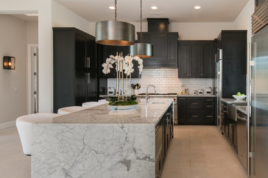 Kitchen - transitional u-shaped gray floor kitchen idea in Phoenix with a farmhouse sink, shaker cabinets, black cabinets, white backsplash, subway tile backsplash, stainless steel appliances, an island and white countertops