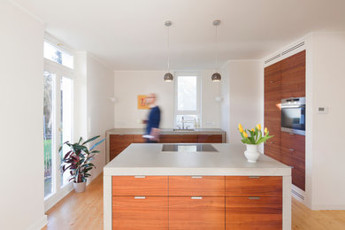 Geschlossene, Mittelgroße Moderne Küche mit integriertem Waschbecken, flächenbündigen Schrankfronten, hellbraunen Holzschränken, Küchengeräten aus Edelstahl, hellem Holzboden und Kücheninsel in Dortmund