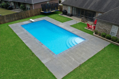 Cette photo montre un grand piscine avec aménagement paysager arrière rectangle avec une dalle de béton.
