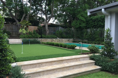 This is an example of a mid-sized contemporary backyard full sun outdoor sport court for summer in Sydney with a retaining wall and natural stone pavers.
