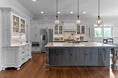Example of a country l-shaped dark wood floor and brown floor kitchen design in Raleigh with a farmhouse sink, shaker cabinets, white cabinets, white backsplash, stainless steel appliances, an island and gray countertops