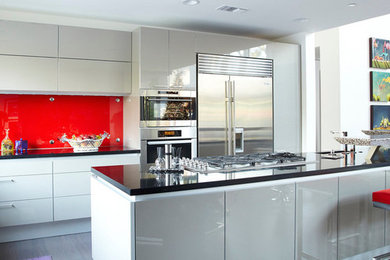 This is an example of a large contemporary l-shaped open plan kitchen in Houston with an undermount sink, flat-panel cabinets, red splashback, metal splashback, white appliances, dark hardwood floors and with island.
