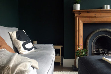 他の地域にある低価格の中くらいなトラディショナルスタイルのおしゃれなリビング (緑の壁、濃色無垢フローリング、標準型暖炉、木材の暖炉まわり、茶色い床、グレーとクリーム色) の写真