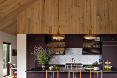 Kitchen - eclectic medium tone wood floor, brown floor and vaulted ceiling kitchen idea in New York with an undermount sink, shaker cabinets, purple cabinets, soapstone countertops, white backsplash, ceramic backsplash, paneled appliances, an island and black countertops