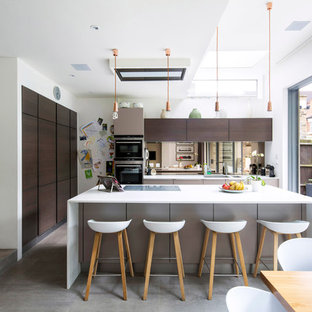 This is an example of a medium sized contemporary l-shaped kitchen/diner in London with a submerged sink, flat-panel cabinets, dark wood cabinets, mirror splashback, an island, grey floors and concrete flooring.