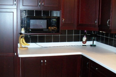 Example of a mid-sized transitional u-shaped eat-in kitchen design in Toronto with an undermount sink, flat-panel cabinets, dark wood cabinets, quartz countertops, black backsplash, ceramic backsplash and black appliances